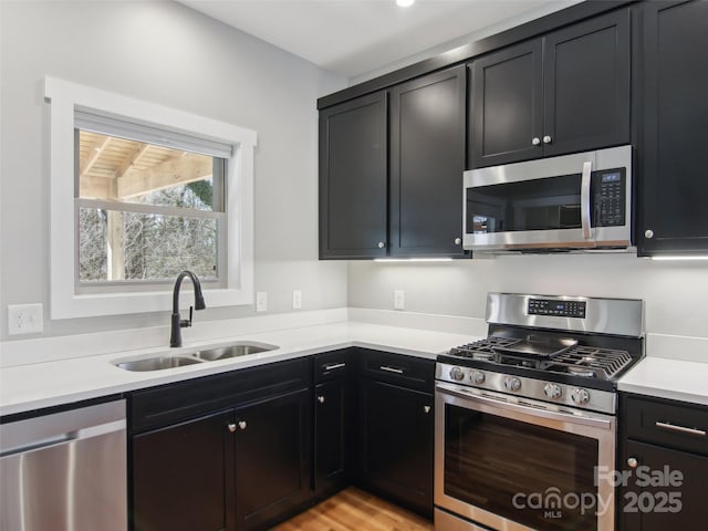 kitchen with appliances with stainless steel finishes, light countertops, a sink, and dark cabinets