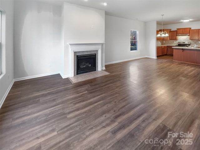 unfurnished living room with a notable chandelier, a fireplace, dark wood finished floors, and baseboards