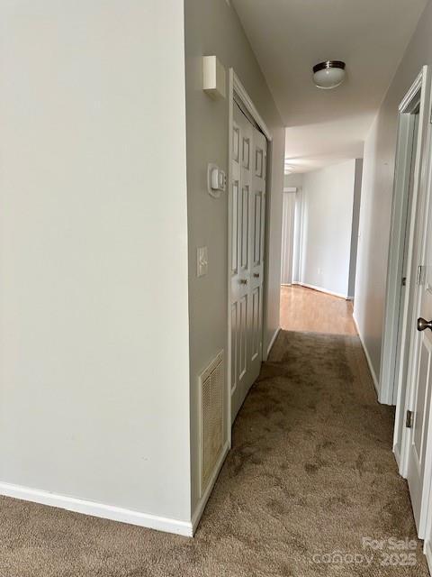 hall with carpet, visible vents, and baseboards