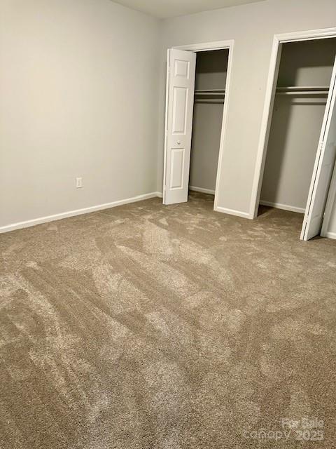 unfurnished bedroom featuring multiple closets, carpet flooring, and baseboards