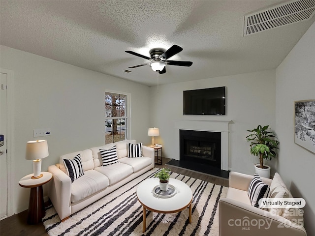 living room featuring ceiling fan, a fireplace, wood finished floors, and visible vents