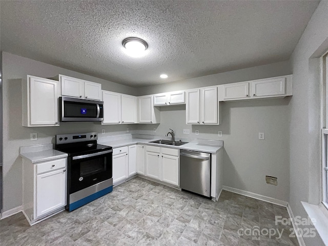 kitchen featuring baseboards, appliances with stainless steel finishes, light countertops, white cabinetry, and a sink