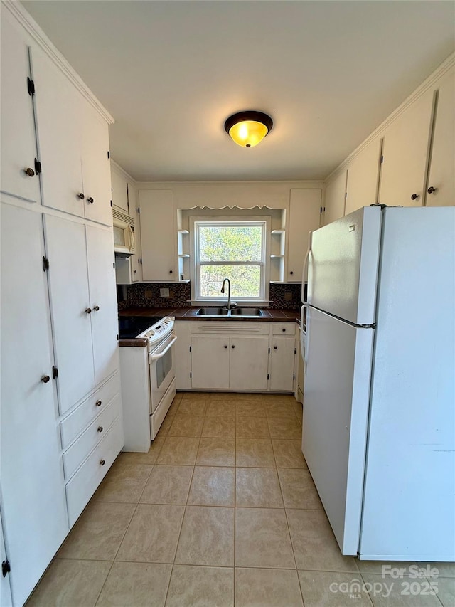 kitchen with white appliances, light tile patterned floors, dark countertops, open shelves, and a sink