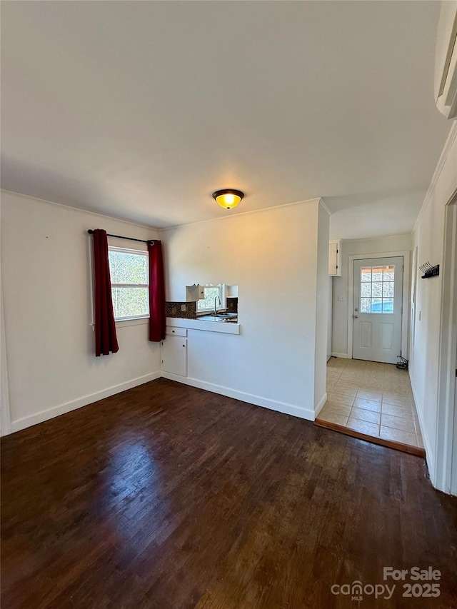 unfurnished living room featuring plenty of natural light, baseboards, wood finished floors, and a wall mounted AC