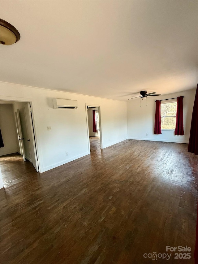 interior space featuring dark wood-style floors, ceiling fan, baseboards, and an AC wall unit