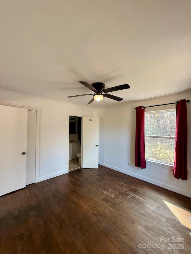 unfurnished bedroom featuring a ceiling fan, baseboards, dark wood-type flooring, and ensuite bathroom