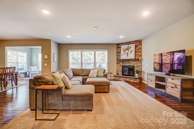 living room featuring a stone fireplace, recessed lighting, wood finished floors, and a healthy amount of sunlight