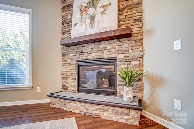 interior details featuring baseboards, a stone fireplace, and wood finished floors