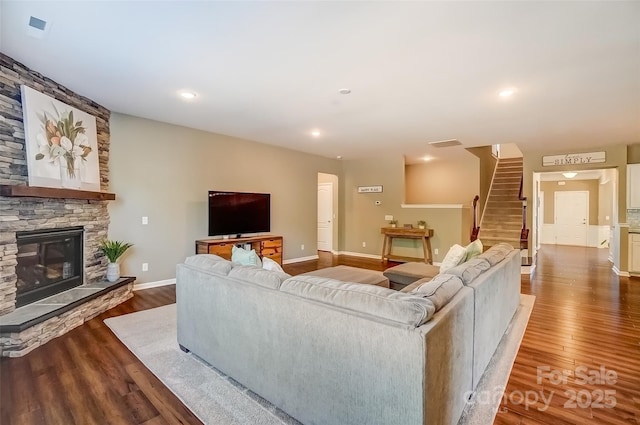 living area featuring visible vents, baseboards, stairs, a stone fireplace, and wood finished floors