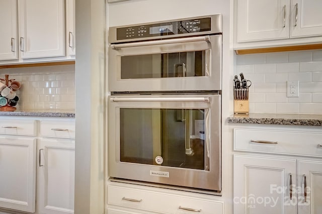 kitchen featuring backsplash, light stone countertops, double oven, and white cabinetry