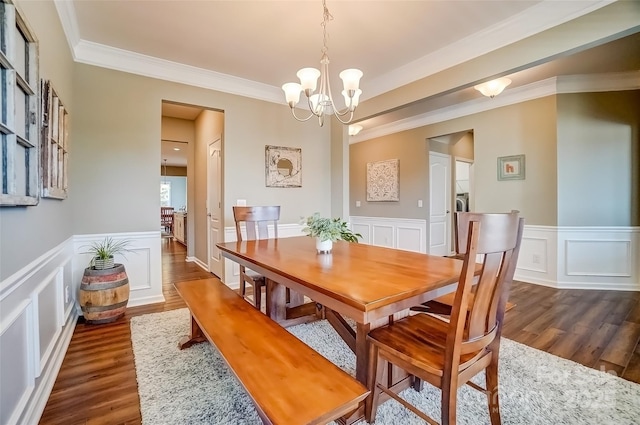 dining room featuring a wainscoted wall, crown molding, dark wood-type flooring, and an inviting chandelier