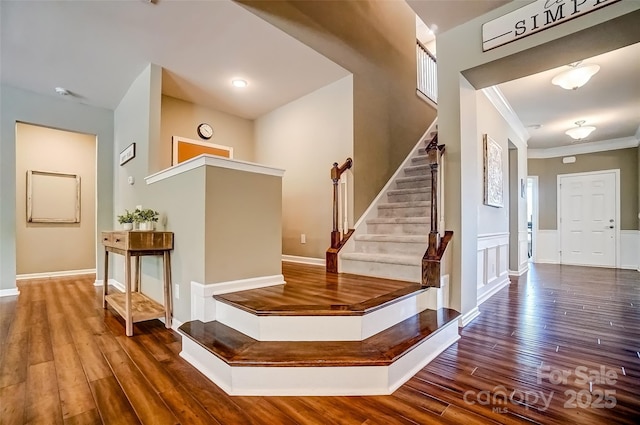 stairway with a wainscoted wall, crown molding, and wood-type flooring