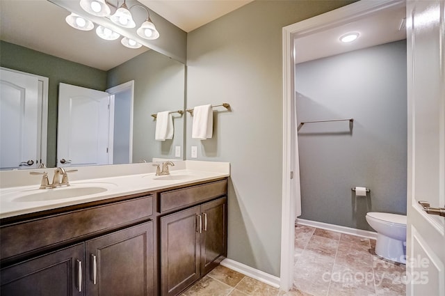 bathroom featuring a sink, baseboards, toilet, and double vanity