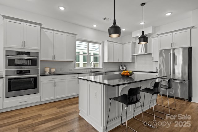 kitchen with stainless steel appliances, dark countertops, visible vents, and a sink