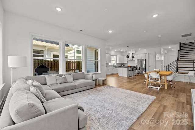 living room with stairway, visible vents, light wood finished floors, and recessed lighting