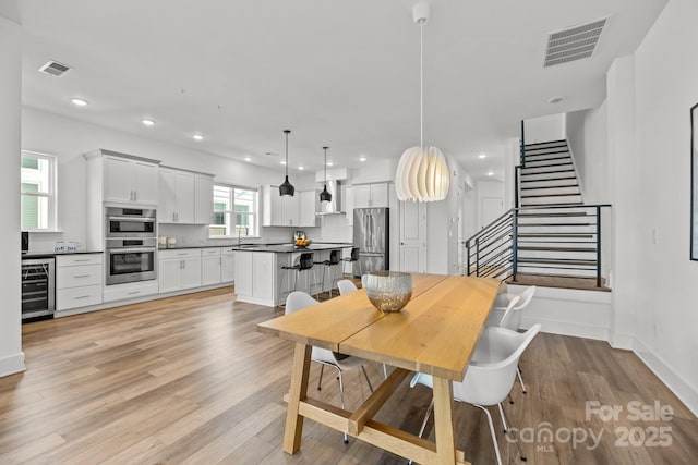 dining area with stairway, wine cooler, visible vents, and light wood-style flooring