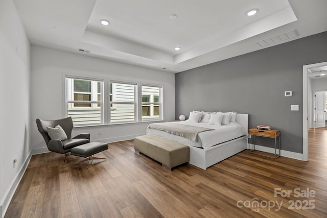 bedroom featuring visible vents, a tray ceiling, and wood finished floors