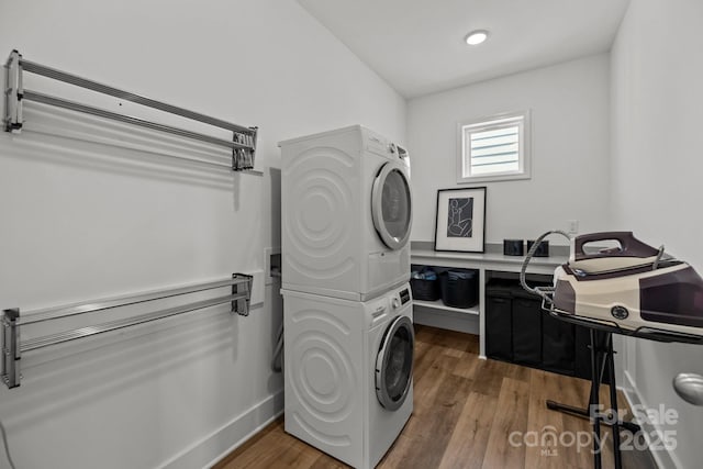 laundry area featuring stacked washer and dryer, laundry area, baseboards, and wood finished floors