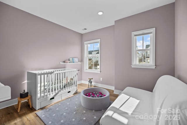 bedroom with a nursery area, visible vents, baseboards, and wood finished floors