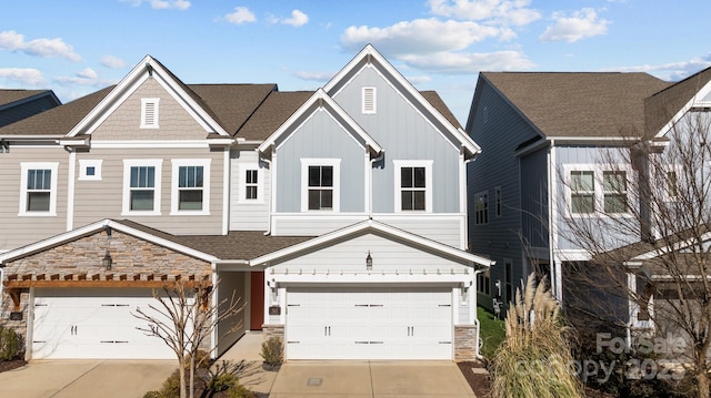 townhome / multi-family property featuring driveway, stone siding, a garage, and board and batten siding