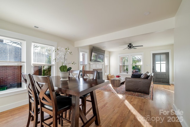 dining area with light wood finished floors, baseboards, a fireplace, and visible vents