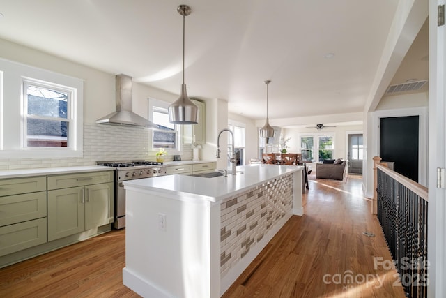 kitchen with green cabinets, stainless steel stove, light wood finished floors, a sink, and wall chimney range hood