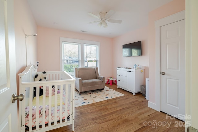bedroom with a crib, light wood-style floors, and ceiling fan