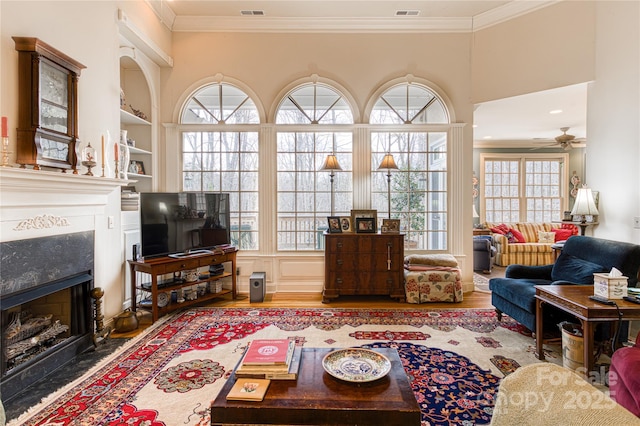 living area featuring ornamental molding, a fireplace with flush hearth, wood finished floors, and built in features