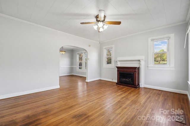 unfurnished living room featuring hardwood / wood-style floors, a healthy amount of sunlight, arched walkways, and baseboards