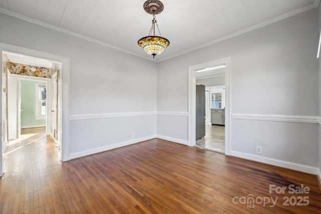 spare room with ornamental molding, an inviting chandelier, baseboards, and hardwood / wood-style flooring