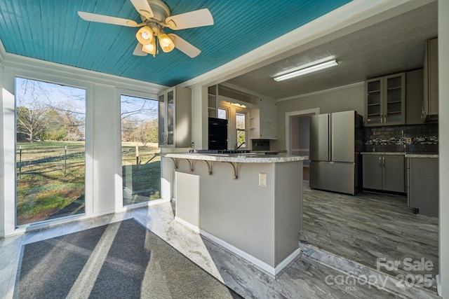 kitchen with a kitchen breakfast bar, tasteful backsplash, freestanding refrigerator, a peninsula, and glass insert cabinets