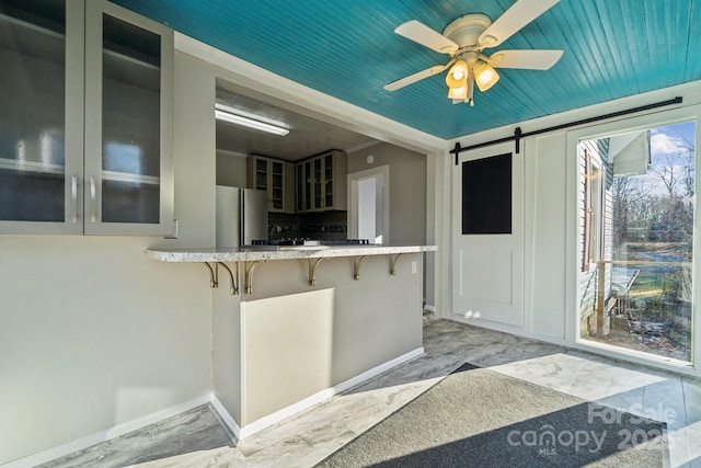 kitchen featuring a breakfast bar, freestanding refrigerator, glass insert cabinets, a barn door, and marble finish floor