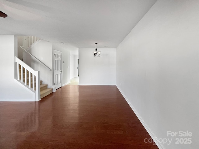 unfurnished room with baseboards, stairway, wood finished floors, and a notable chandelier