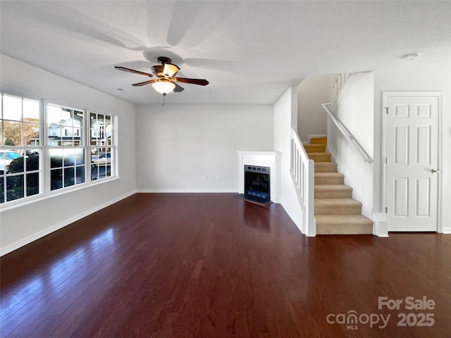 unfurnished living room with baseboards, a fireplace with flush hearth, ceiling fan, stairway, and wood finished floors