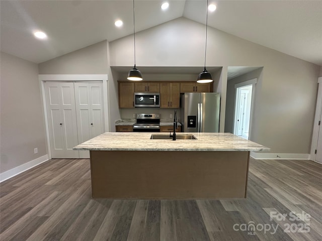 kitchen with dark wood-style flooring, pendant lighting, a center island with sink, appliances with stainless steel finishes, and a sink