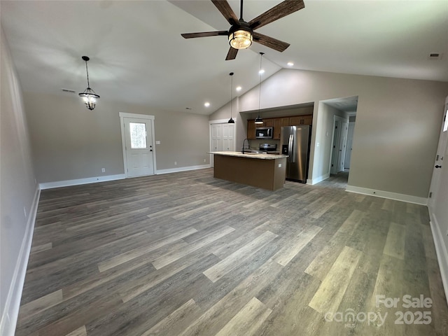 kitchen featuring stainless steel appliances, wood finished floors, open floor plan, light countertops, and a center island with sink