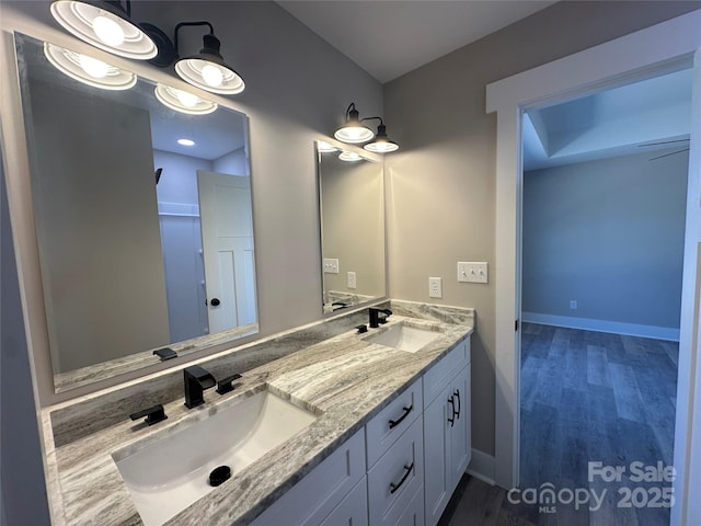 full bathroom featuring wood finished floors, a sink, baseboards, and double vanity