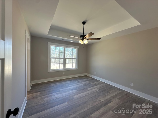 unfurnished room featuring ceiling fan, a tray ceiling, dark wood-type flooring, and baseboards