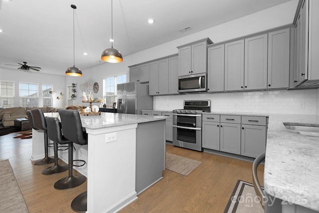 kitchen featuring appliances with stainless steel finishes, gray cabinets, wood-type flooring, and tasteful backsplash