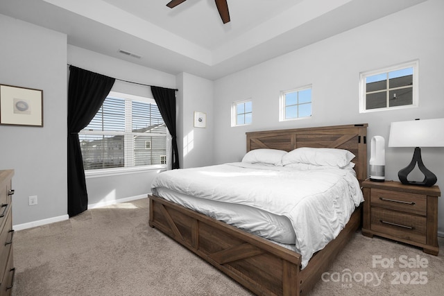 bedroom featuring visible vents, multiple windows, baseboards, and a tray ceiling