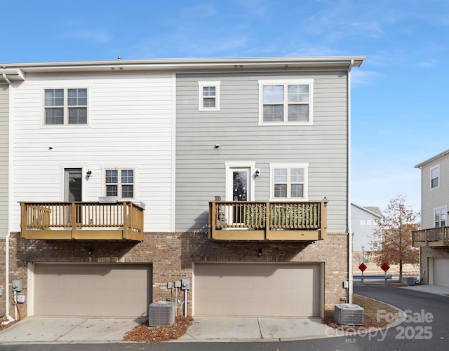 back of house featuring a garage, brick siding, a balcony, and central AC unit