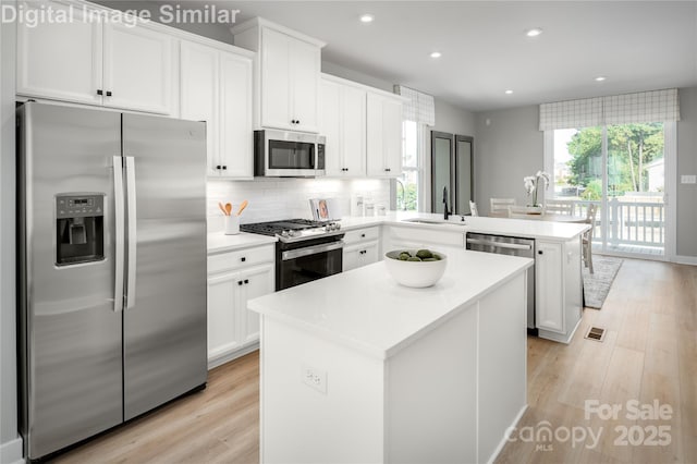 kitchen with a center island, backsplash, appliances with stainless steel finishes, a sink, and a peninsula