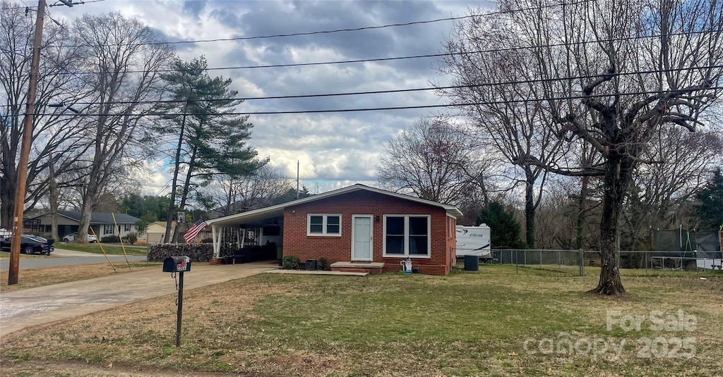 view of front of house with brick siding, concrete driveway, fence, a carport, and a front yard