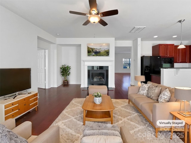 living area featuring ceiling fan, wood finished floors, visible vents, baseboards, and a glass covered fireplace