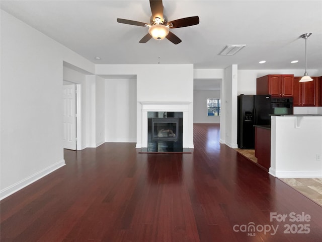 unfurnished living room with ceiling fan, a fireplace with flush hearth, wood finished floors, visible vents, and baseboards