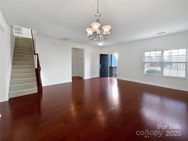 unfurnished room with a chandelier, wood finished floors, visible vents, baseboards, and stairway