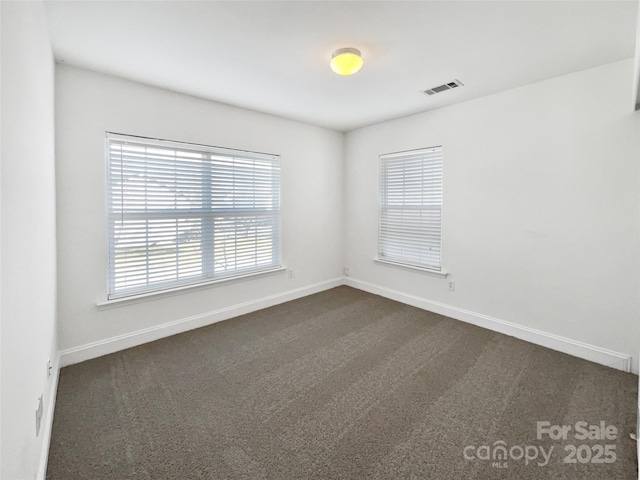 empty room featuring baseboards, visible vents, and dark colored carpet