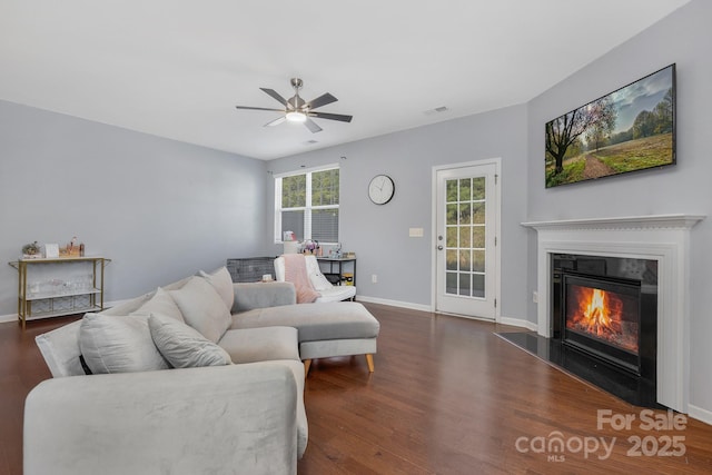 living area with visible vents, a glass covered fireplace, ceiling fan, wood finished floors, and baseboards