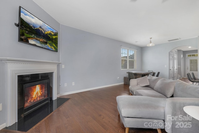 living room featuring arched walkways, visible vents, a glass covered fireplace, wood finished floors, and baseboards