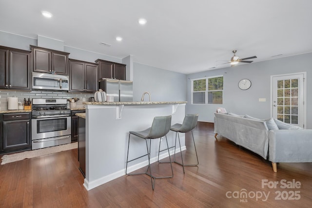 kitchen with dark brown cabinetry, open floor plan, appliances with stainless steel finishes, tasteful backsplash, and a kitchen bar